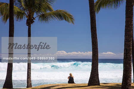 Female tourist sitting on beach looking out at Indian Ocean, Reunion Island