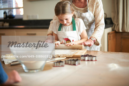 Senior woman and granddaughter rolling dough for Christmas tree cookies