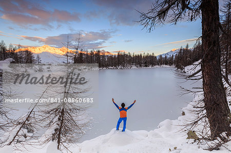 Hiker admires Lago Azzurro completely frozen at dawn, Spluga Valley, Province of Sondrio, Valtellina, Lombardy, Italy, Europe