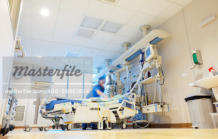 A hospital room with modern medical equipment and blurred patient and nurse or doctor figures.