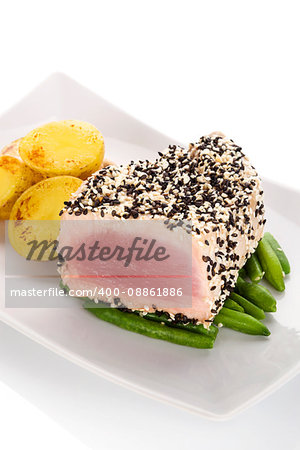 Grilled tuna steak wrapped in black and white sesame seeds on green beans with potatoes on white plate on white background. Culinary seafood eating.