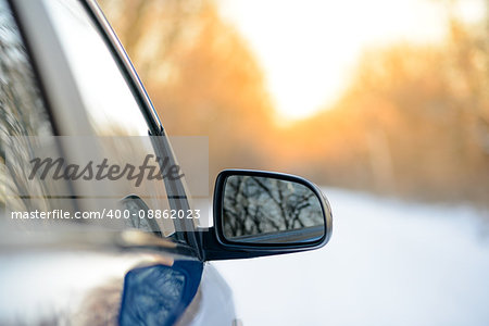 Close up Image of Side Rear-view Mirror on a Blue Car in the Winter Landscape with Evening Sun