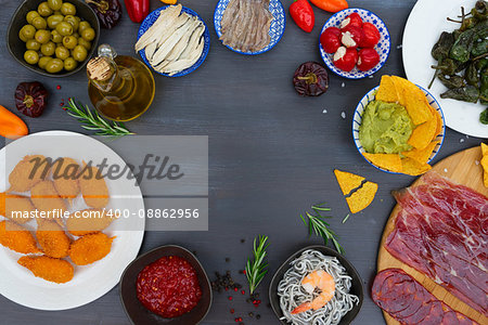 Table with spanish tapas food - anchovies with peppers padron, jamon, croquetes, guacamole and olives, frame with copy space