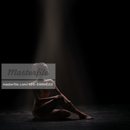 silhouette of beautiful woman ballet dancer sitting on wooden floor over dark background