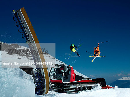 Skiers jumping piste machine