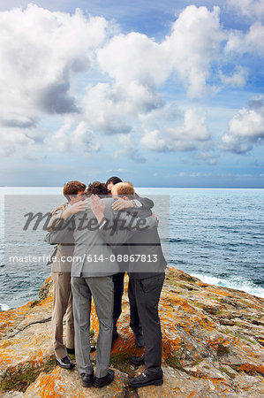 Businessmen talking in huddle on cliff