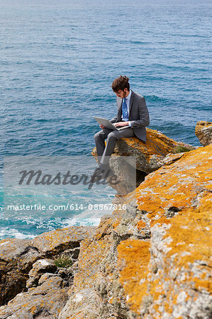 Businessman using laptop on cliff