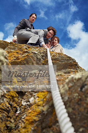 Businessmen pulling rope over cliff