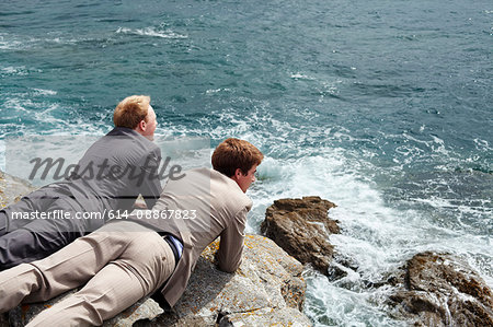 Businessmen peering over cliff edge
