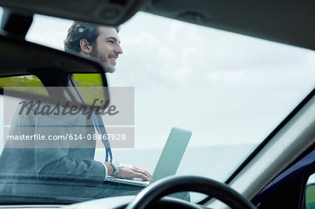 Businessman using laptop on hood of car