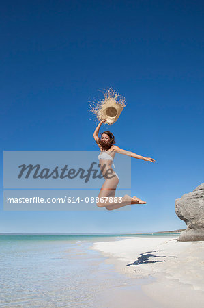 Woman jumping with straw hat on beach