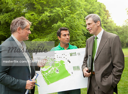 Businessmen examining blueprints in park