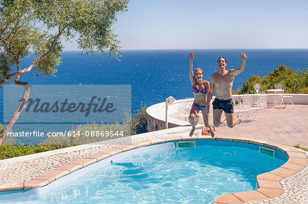 Couple jumping into swimming pool