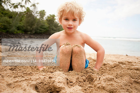 Young boy with feet buried in sand on beach, portrait