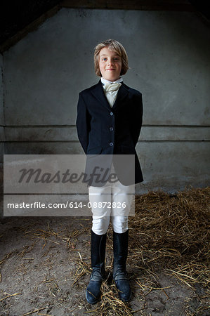 Boy standing in horse riding clothes in stable