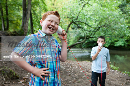 Two boys using paper cups and string to communicate in woodland