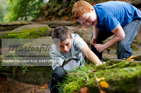 Two boys looking through a magnifying glass in a woodland