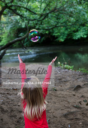 Girl reaching to catch a bubble in a woodland setting