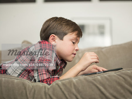 Boy playing with digital tablet on sofa, side view