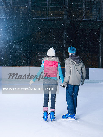 Couple holding hands on the ice rink watching the snow falling