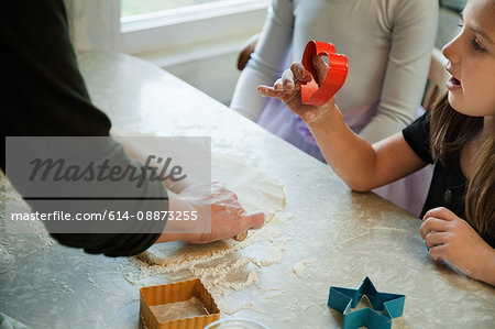 Mother helping girls in kitchen to bake cookies