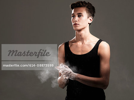 Young athlete rubbing powder on hands against grey background