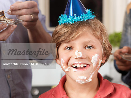 Portrait of boy in party hat with cake smeared on face