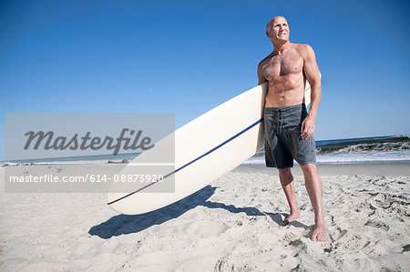 Surfer standing with surfboard on beach