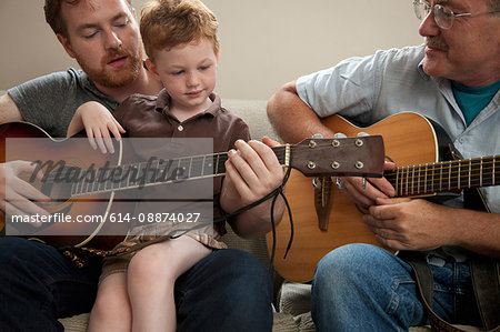 Father teaching son to play guitar, with grandfather
