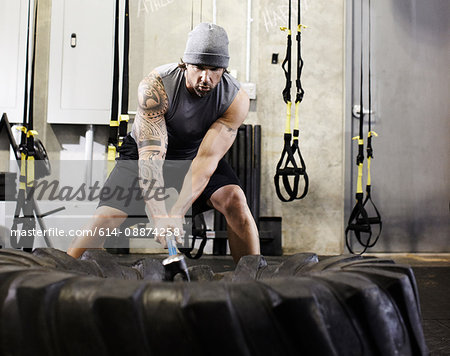 Man hitting tyre with sledgehammer in a gym