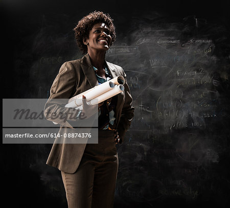 Businesswoman holding blueprint by blackboard