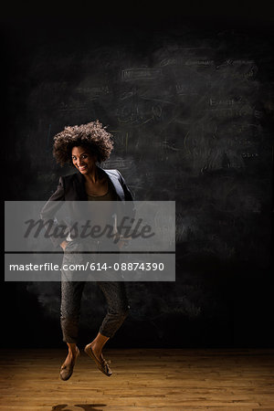 Businesswoman jumping by blackboard