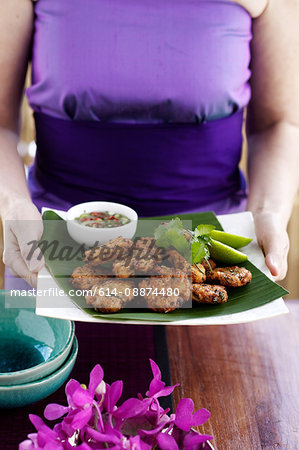Woman carrying fishcake appetisers with coriander, lime and hot sour dipping sauce