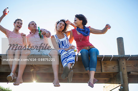 Young friends sitting together on jetty, low angle view