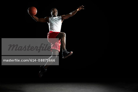 Young male basketball player jumping with ball