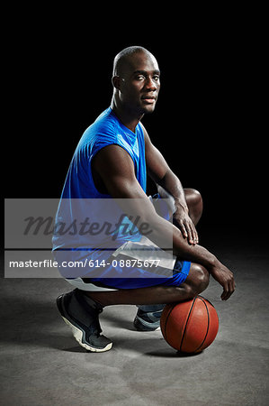 Studio portrait of basketball player kneeling on ball