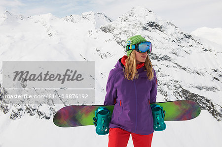 Young woman holding snowboard at top of mountain