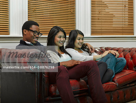 Three young adult friends sitting on sofa together