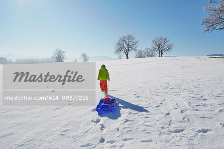 Young boy walking in snow, pulling sled behind him, rear view