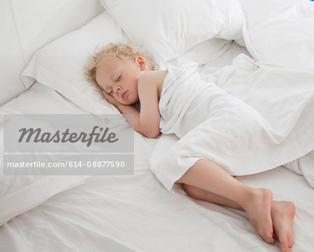 Young boy asleep on bed, under cover