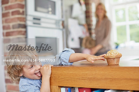 Young boy trying to reach muffin on kitchen counter