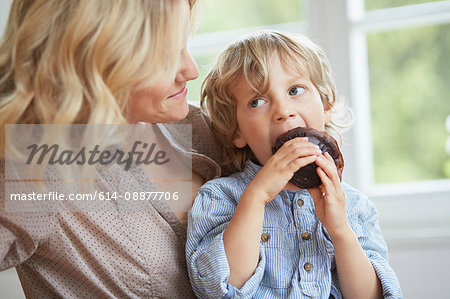 Young boy seating chocolate muffin whilst his mother looks on