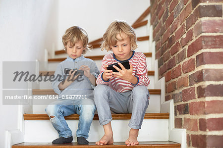 Two young brothers sitting on stairs, looking at smartphones