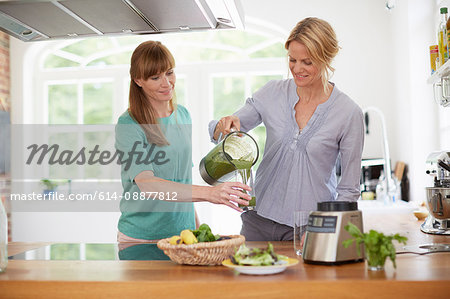 Women drinking green vegan smoothie in kitchen