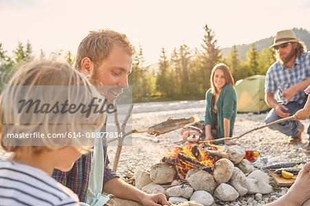Family sitting around campfire cooking fish attached to branch