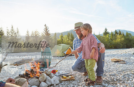 Boy and mid adult man poking campfire with branch