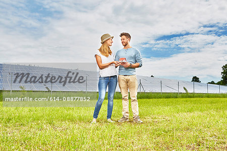 Young couple standing in field, holding small model of house, next to solar farm