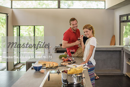 Couple preparing food and drinking red wine in kitchen