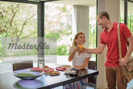 Young woman handing orange juice to boyfriend at breakfast table