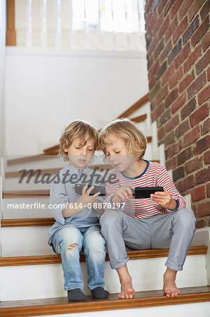 Two young boys, sitting on stairs, looking at smartphones